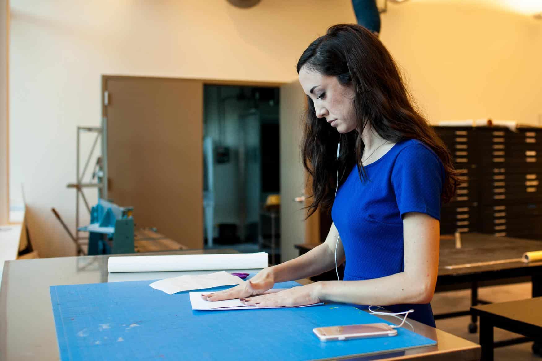 Young woman at a standing desk, working with paper in an art setting