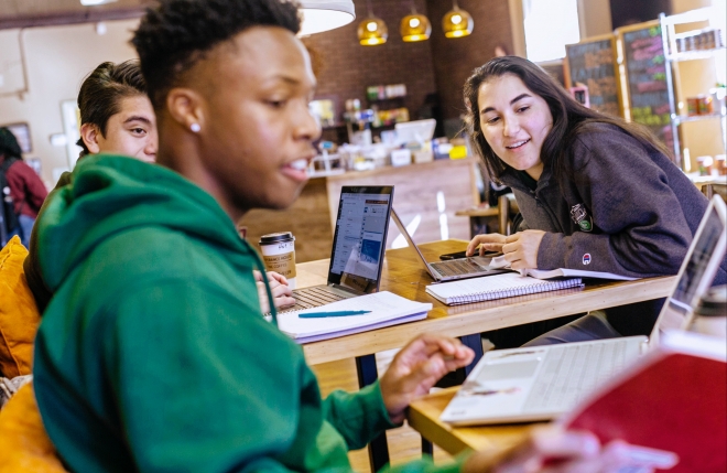 Students sitting together looking at one student's laptop