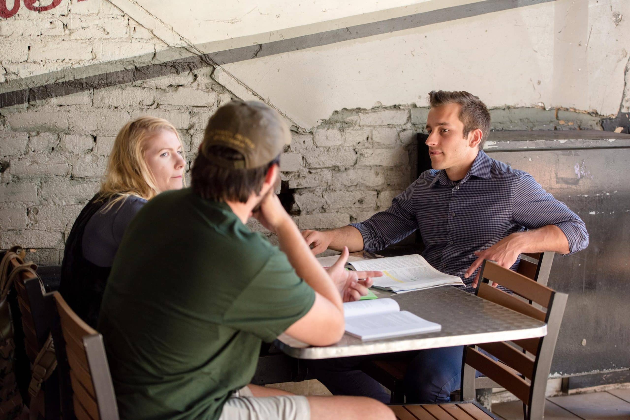 Three students discussing school work sitting at a table in front of a gray brick wall