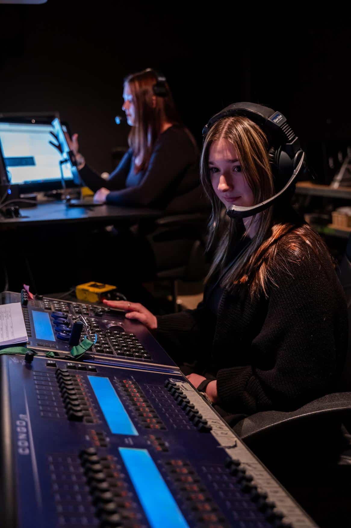 Two young ladies in front of sound and lighting boards, wearing headsets