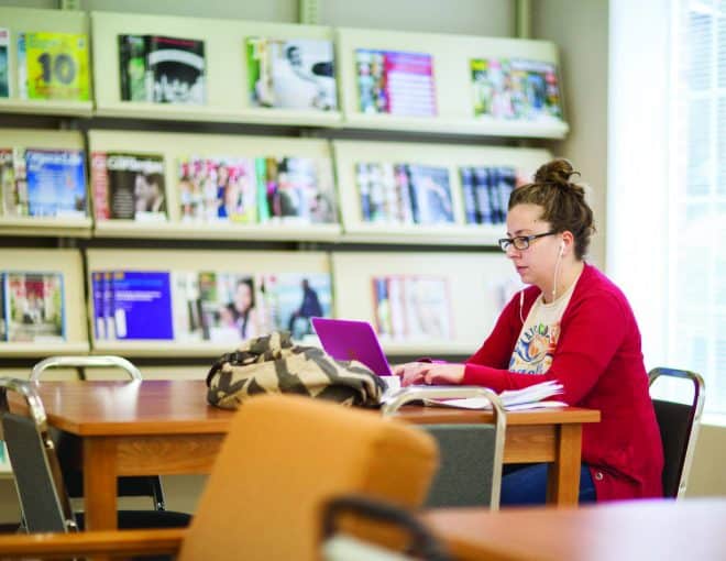 Young woman with headphones in, working on her laptop in a library