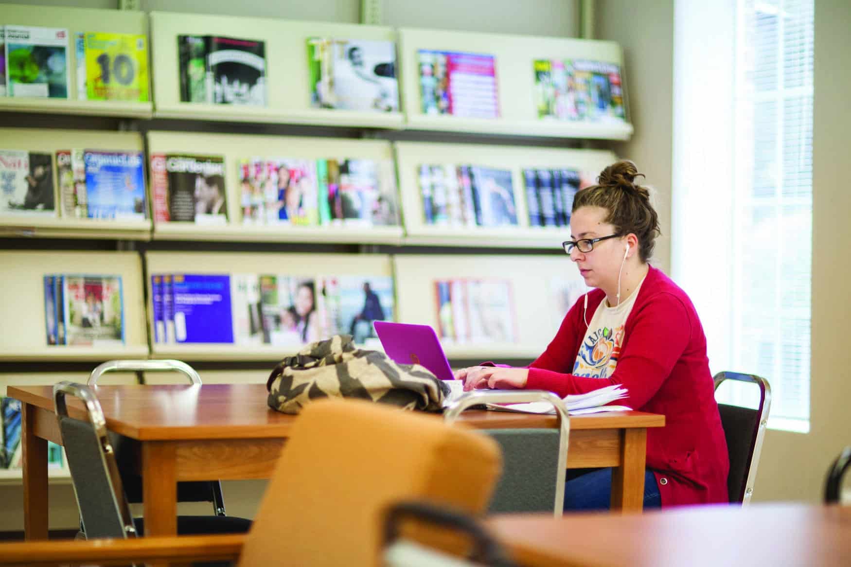 Young woman with headphones in, working on her laptop in a library
