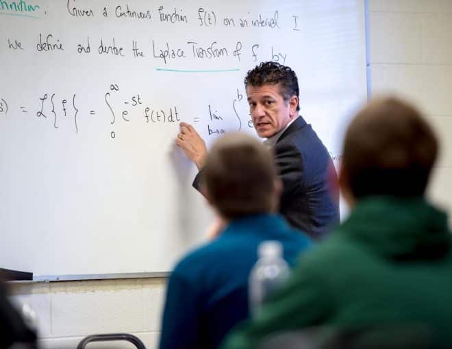 Professor teaching a math formula to students on a white board.