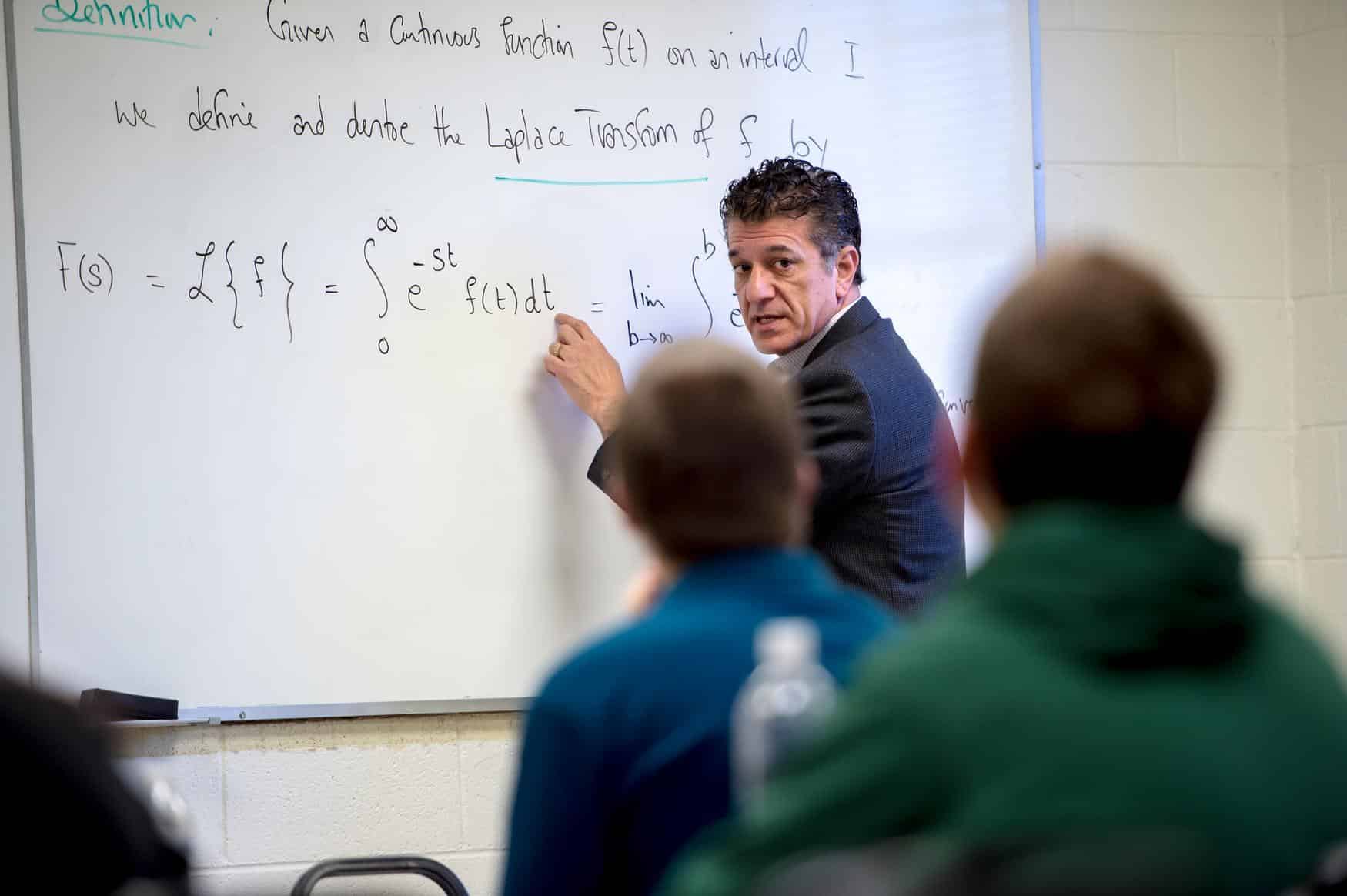 Professor teaching a math formula to students on a white board.