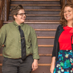 Two adults standing on wooden stairs in an art gallery, smiling