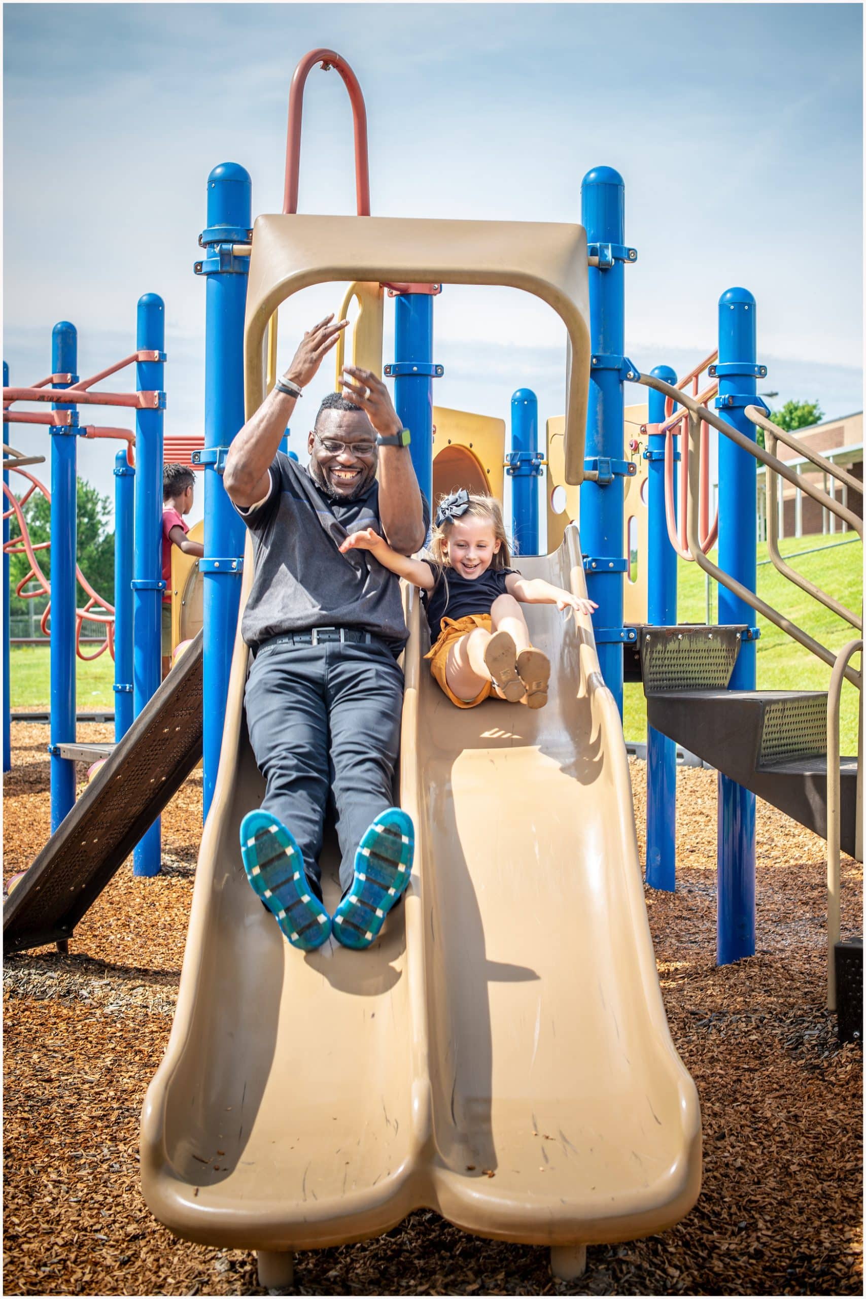 Young man and child smiling and going down a slide on a playground