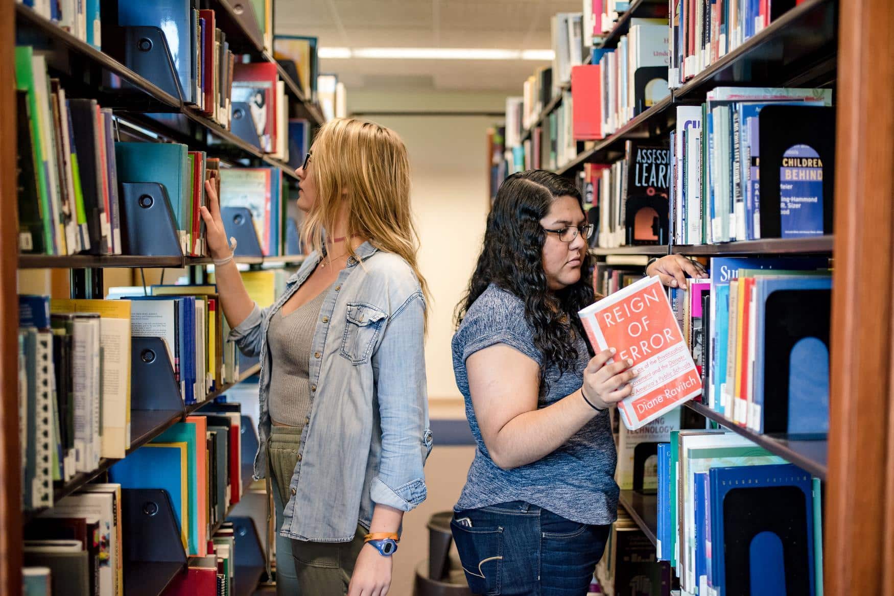 Two young women in the library. They are filing books.