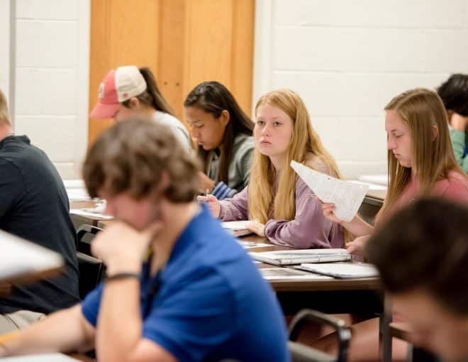 Candid photograph of students in history class, reading and listening to the lecture.