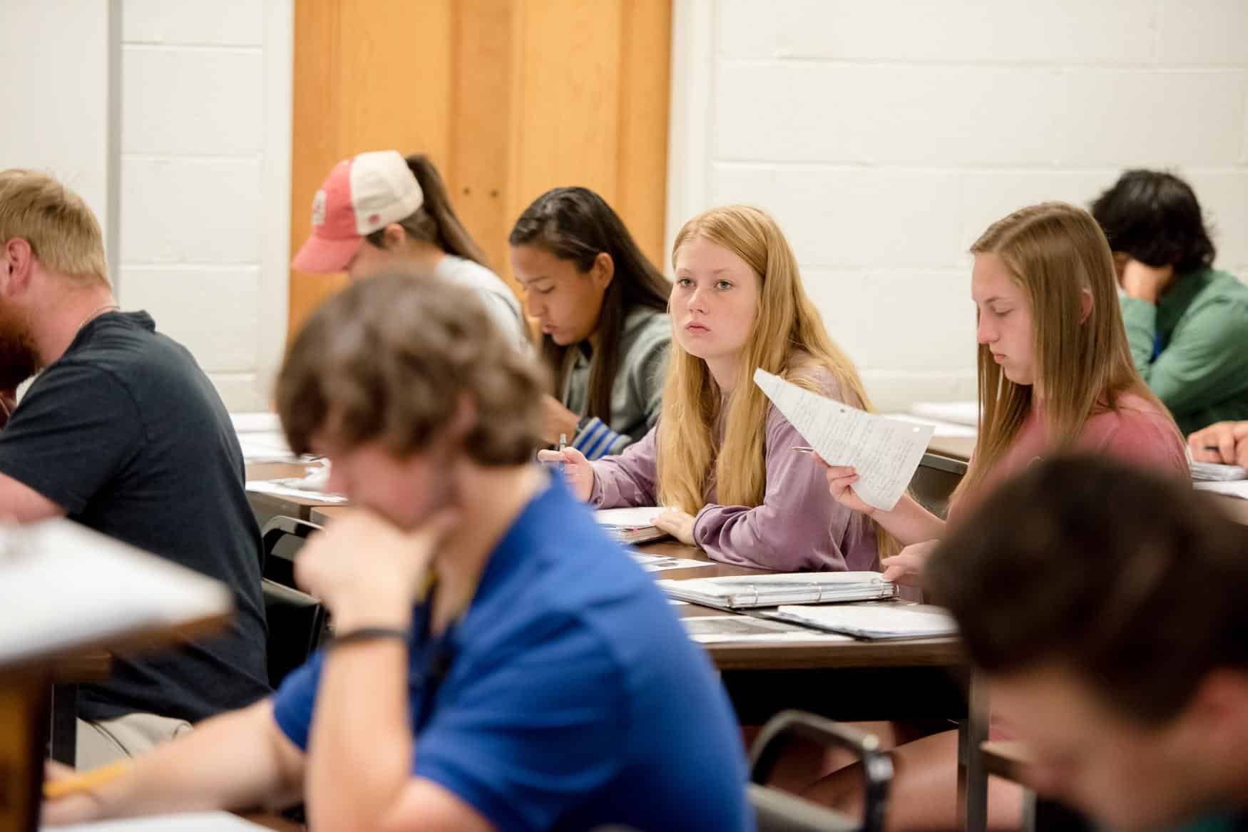 Candid photograph of students in history class, reading and listening to the lecture.