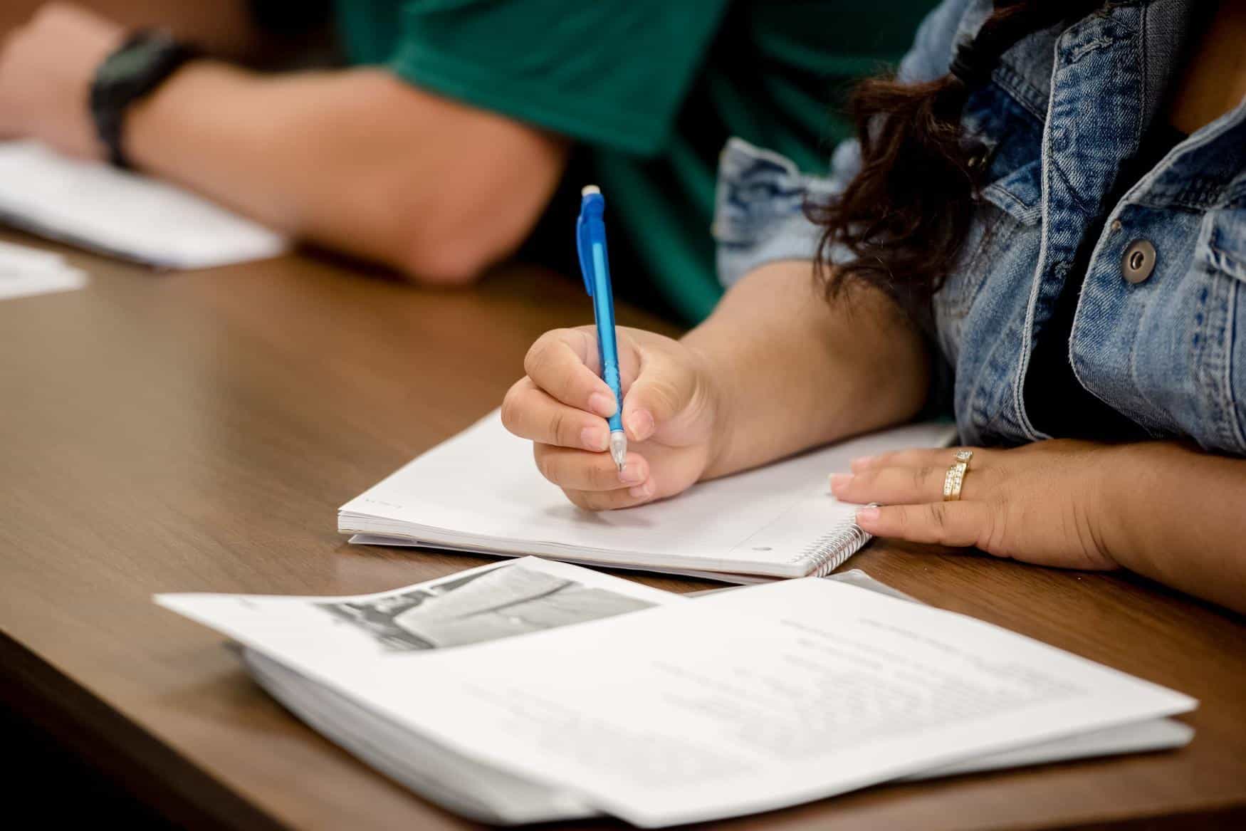 Close-up view of a student writing notes and reading class papers.