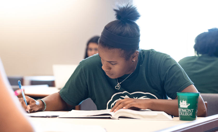 Student wearing a green Piedmont shirt, leaning over a book studying