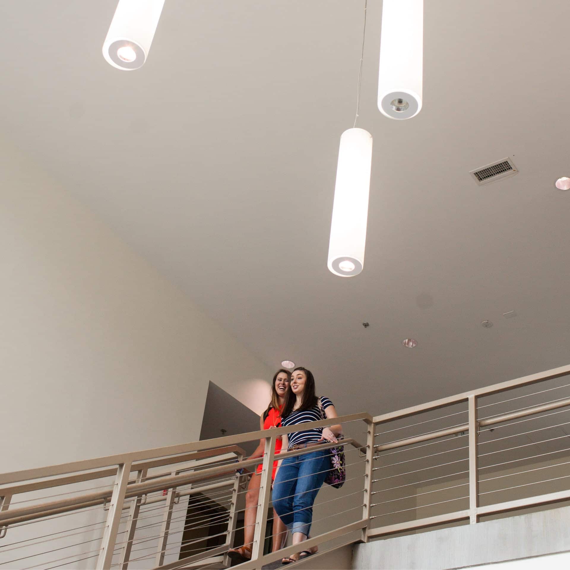 Two young women walking down stairs, with the ceiling and pendant lights visible