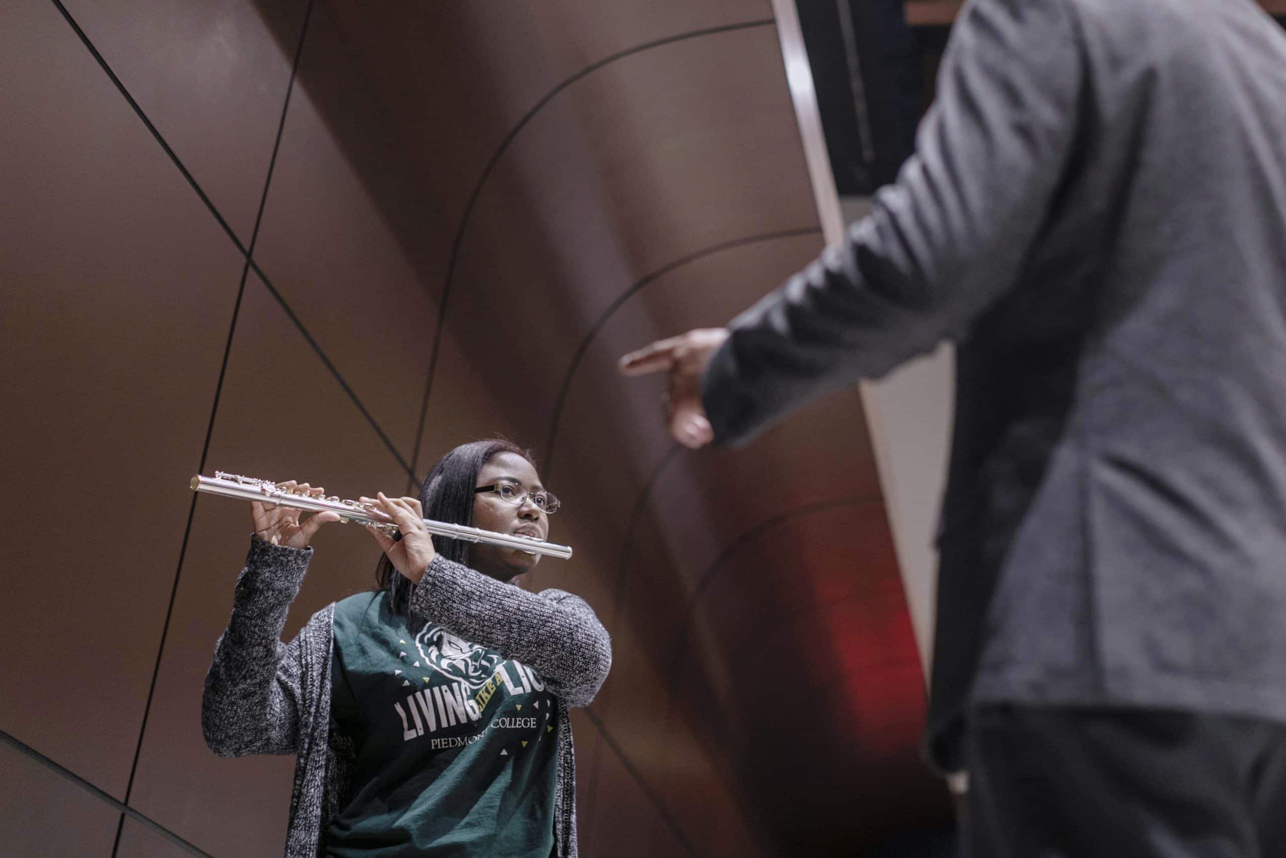 Young woman playing flute while looking at a conductor