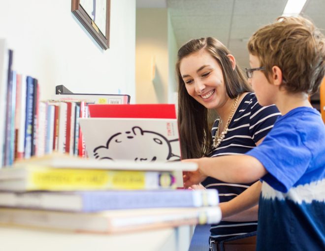Young woman talking with a little boy, looking at a book together
