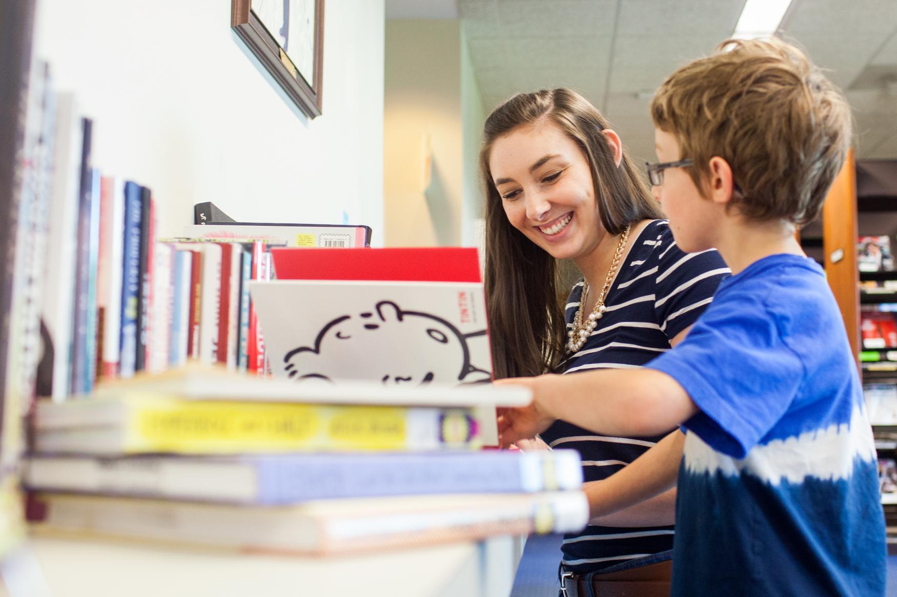 Young woman talking with a little boy, looking at a book together