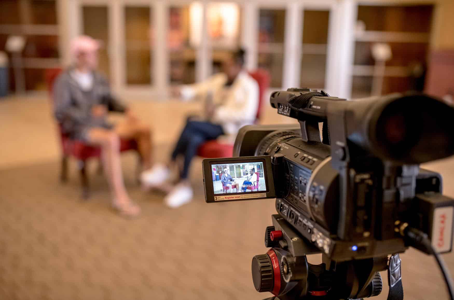 Close up view of a video camera recording. The subjects being videoed are out of focus in the background.