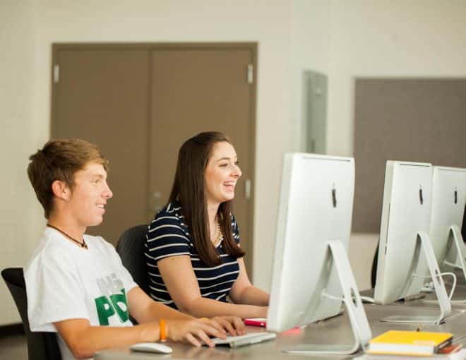 Young man and young women in a computer lab, laughing together.
