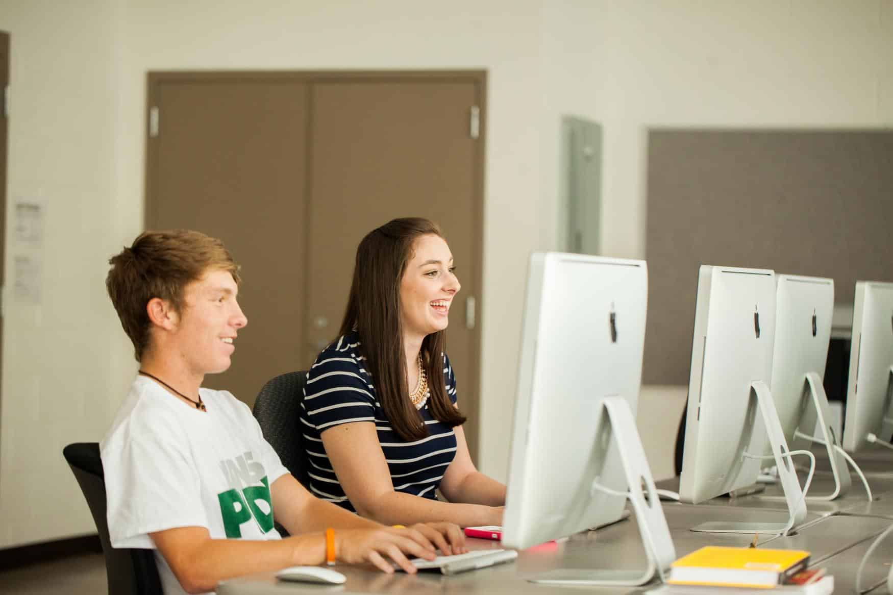 Young man and young women in a computer lab, laughing together.