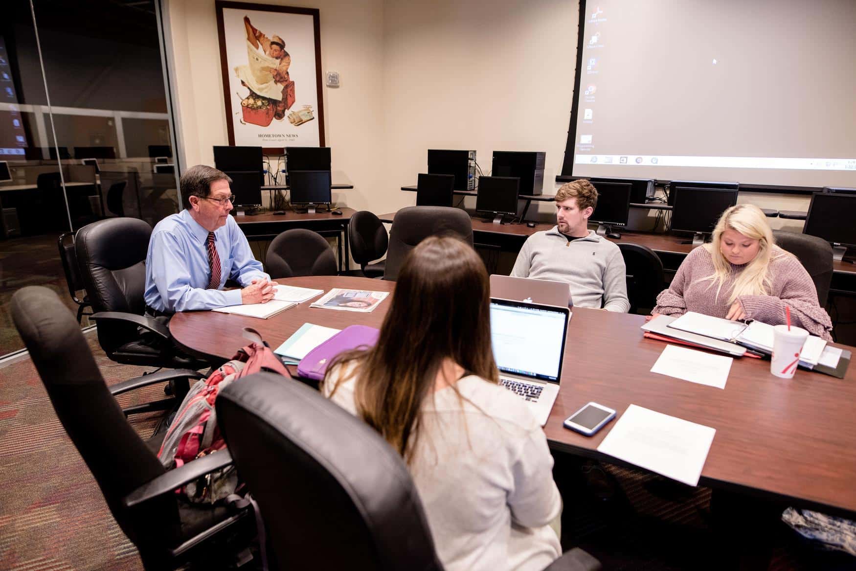 People sitting at a wooden conference table with notes and laptops.