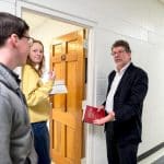 A candid photo of three adults holding books and paper, in the middle of a discussion