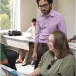 A professor in conversation with a student, both are looking at a laptop