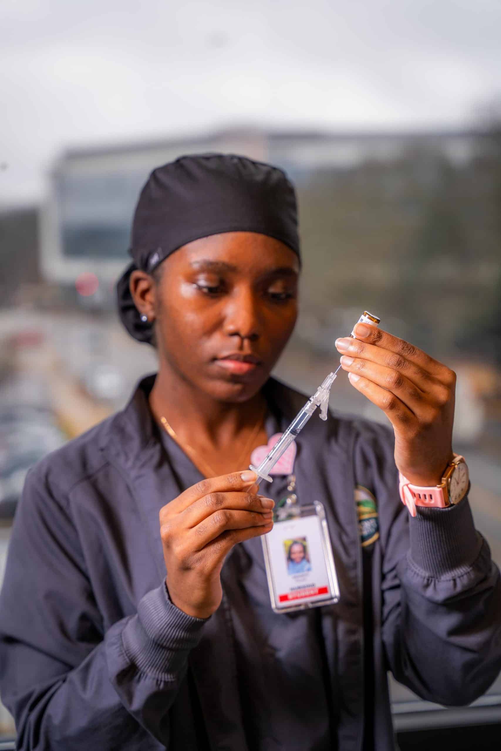 A nursing student taking medicine from a vial into a syringe