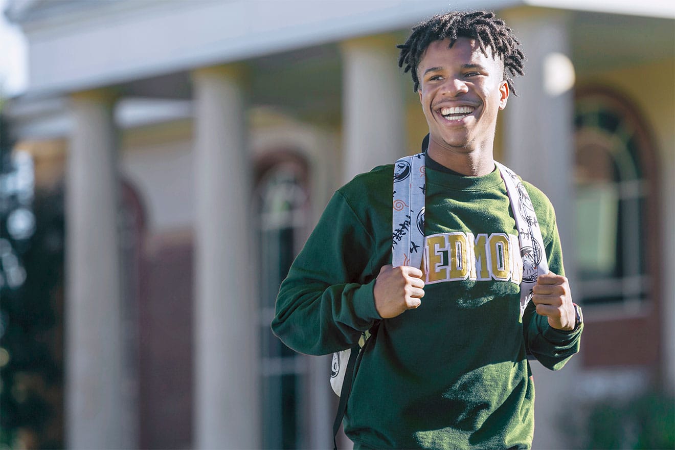 Young man wearing a green sweatshirt walking across campus
