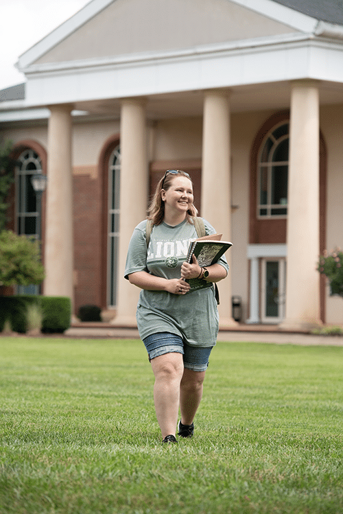 Young woman holding books walking across campus