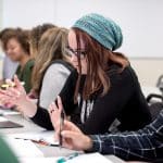 Row of students taking notes and writing on paper.