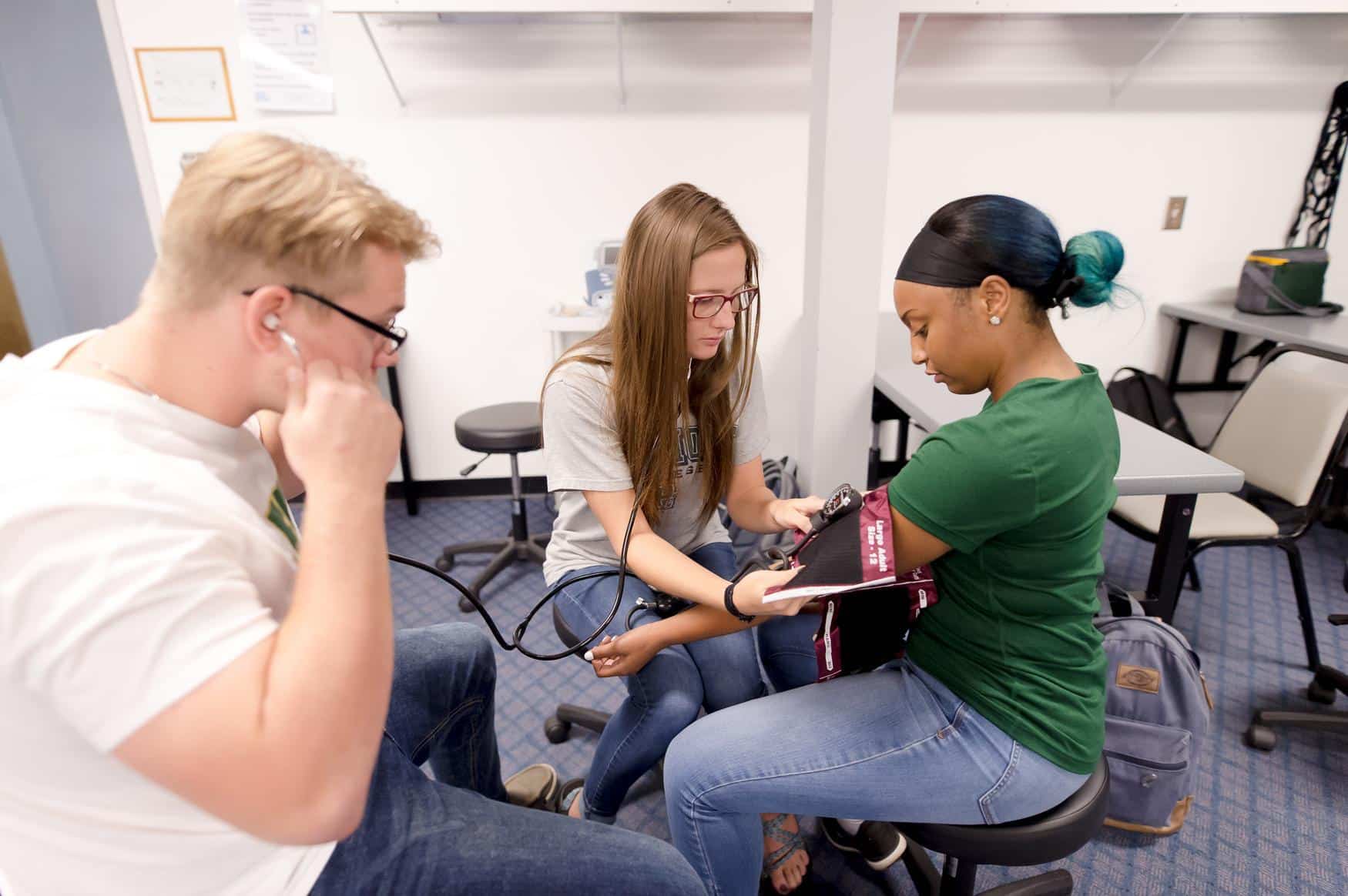 Two students sit and take the blood pressure of a third student.
