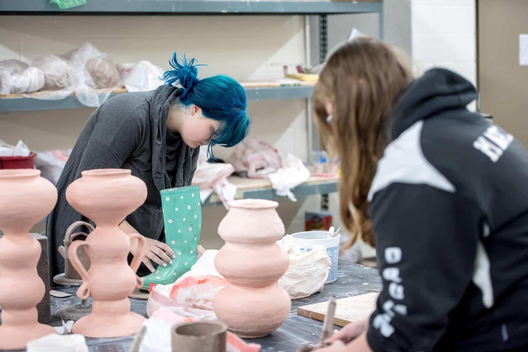 Two students in a ceramic studio, working with pottery