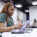 Young woman in a green Piedmont shirt making notes on a tablet