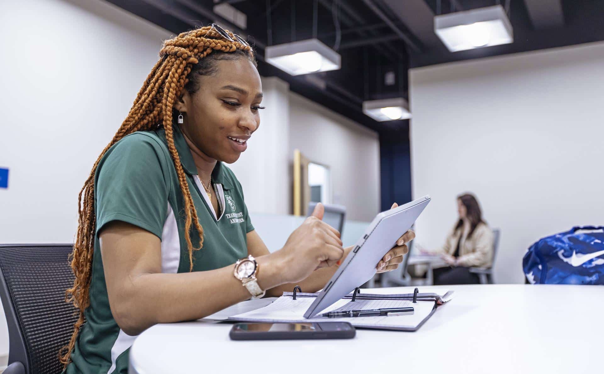 Young woman in a green Piedmont shirt making notes on a tablet