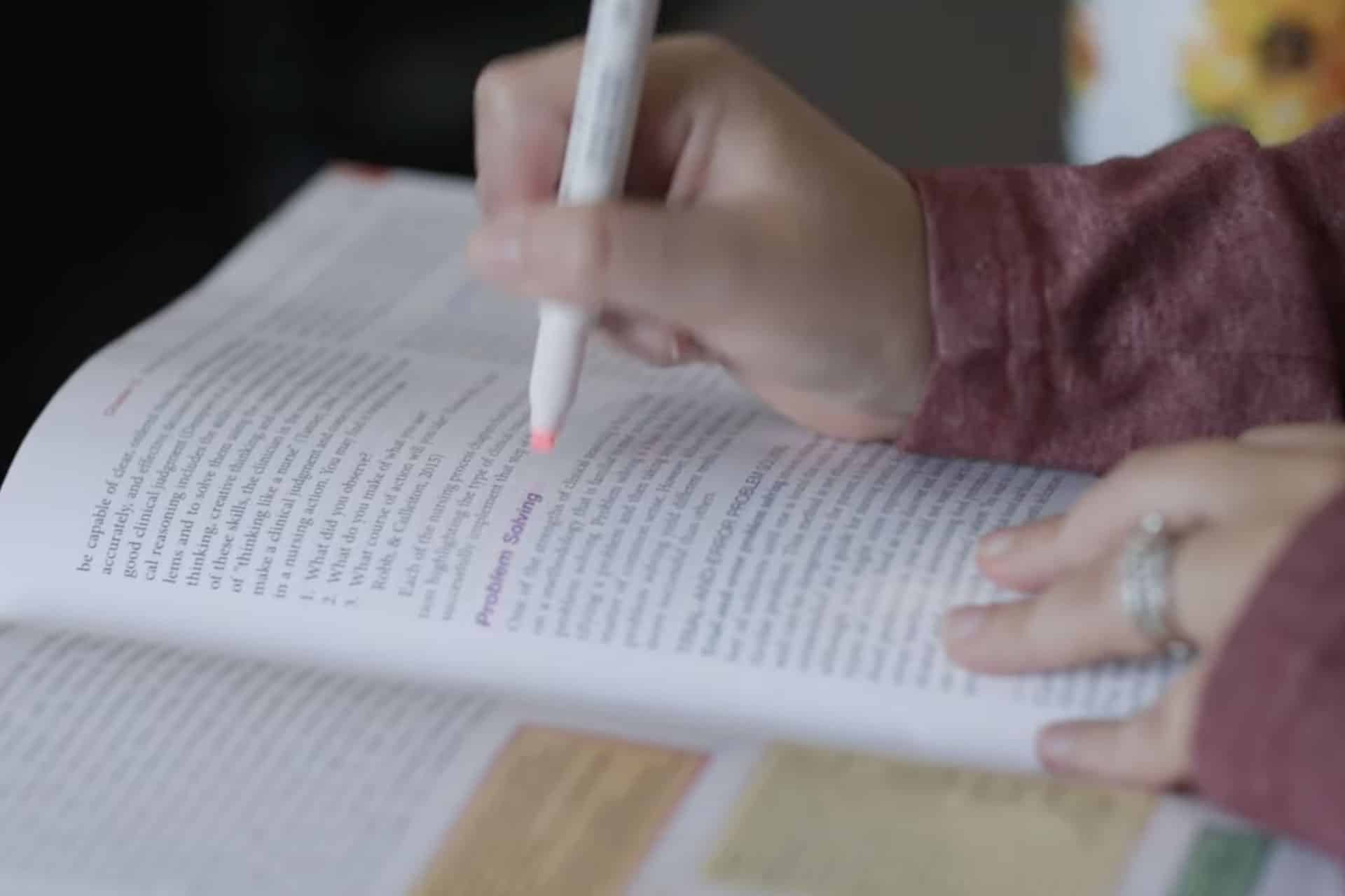 Close up video of hands holding a highlighting pen making marks in a textbook.