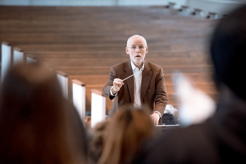 Music conductor leading a group of students. Pews can be seen in the background.