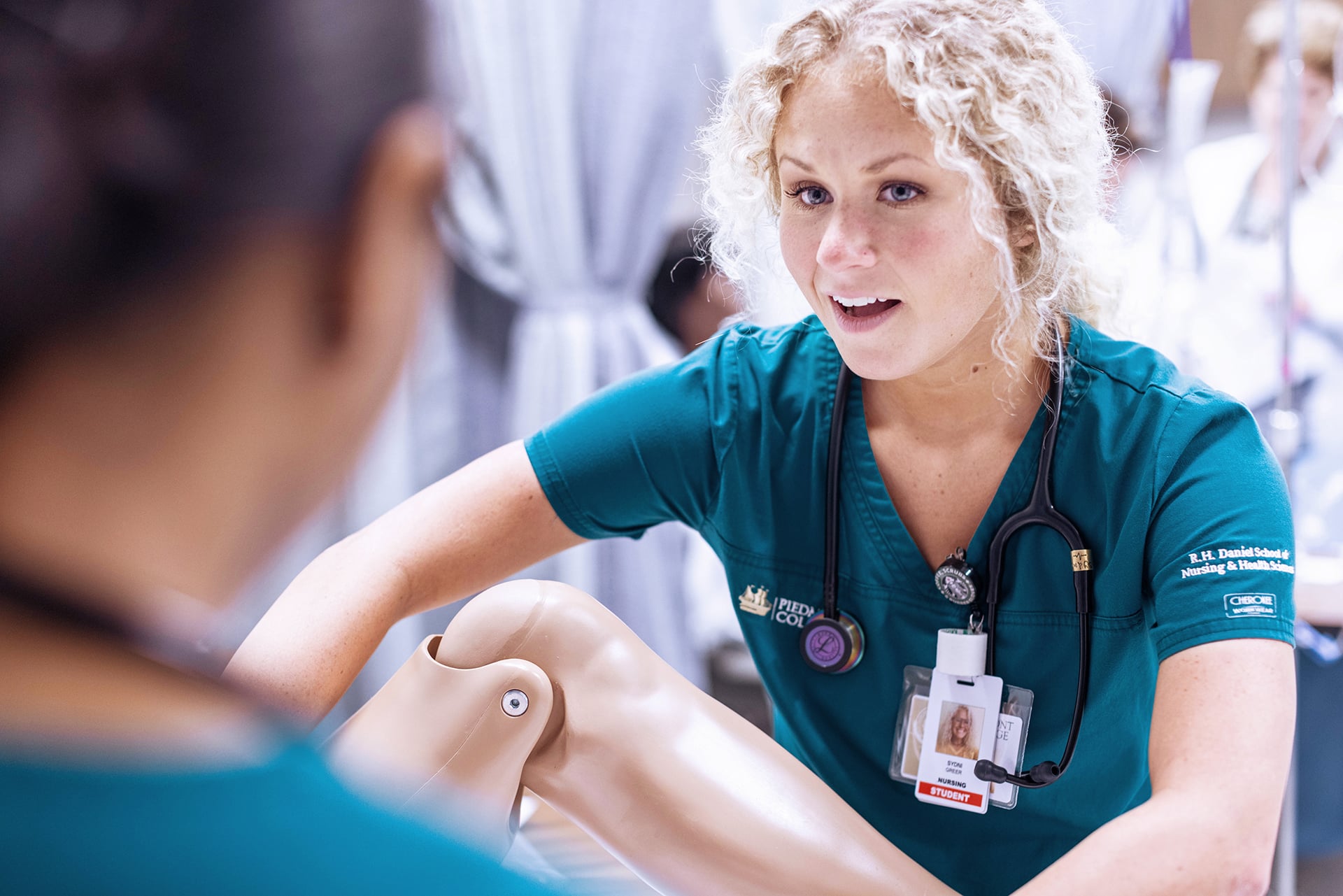 A nursing student holding a prosthetic leg, speaking to another student