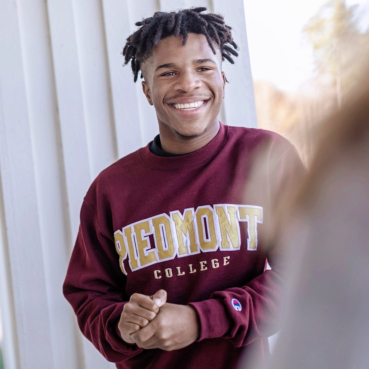 A young man wears a red Piedmont college sweater and smiles