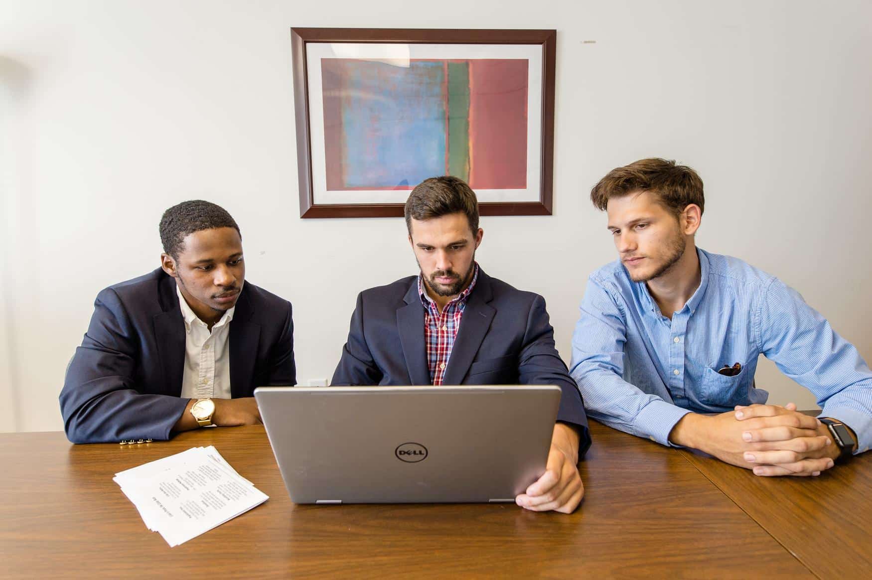 Three young men are intently focused on a laptop in front of them