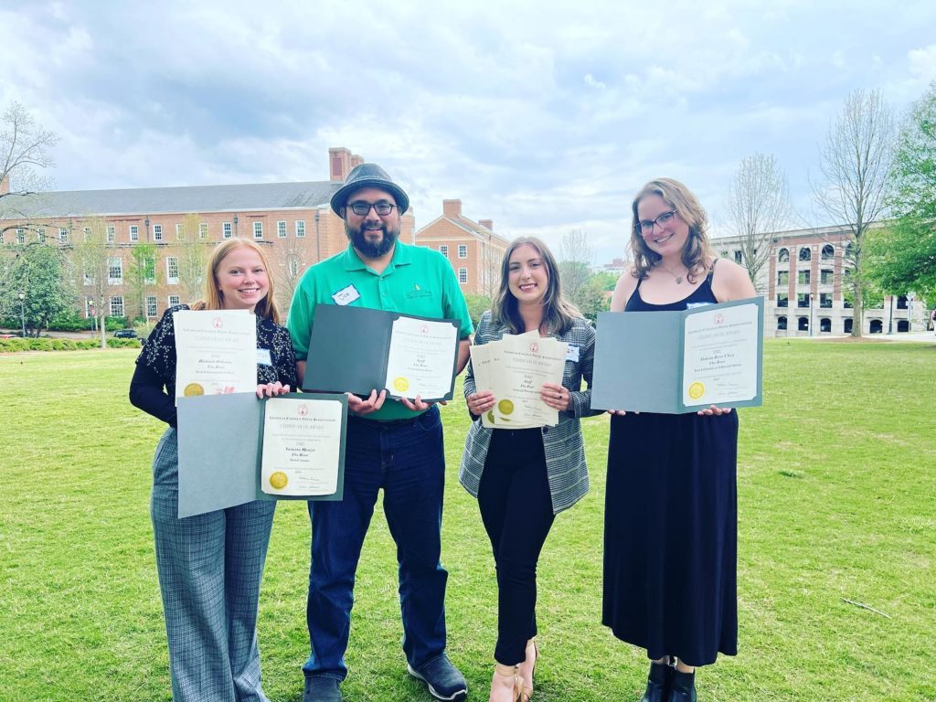Student with their professor and awards for the student newspaper
