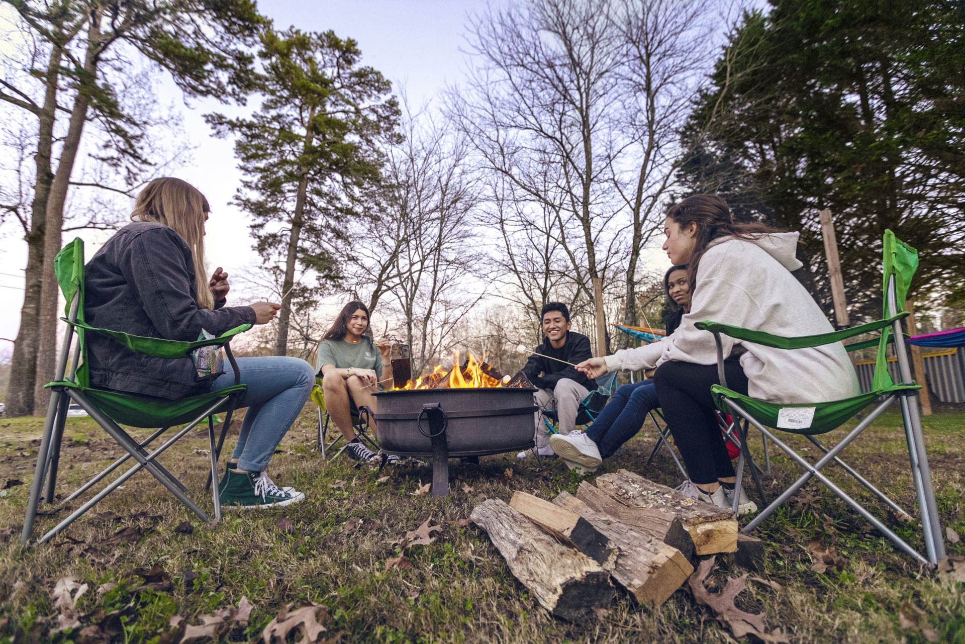 Group of students in folding camping chairs, sitting around a fire