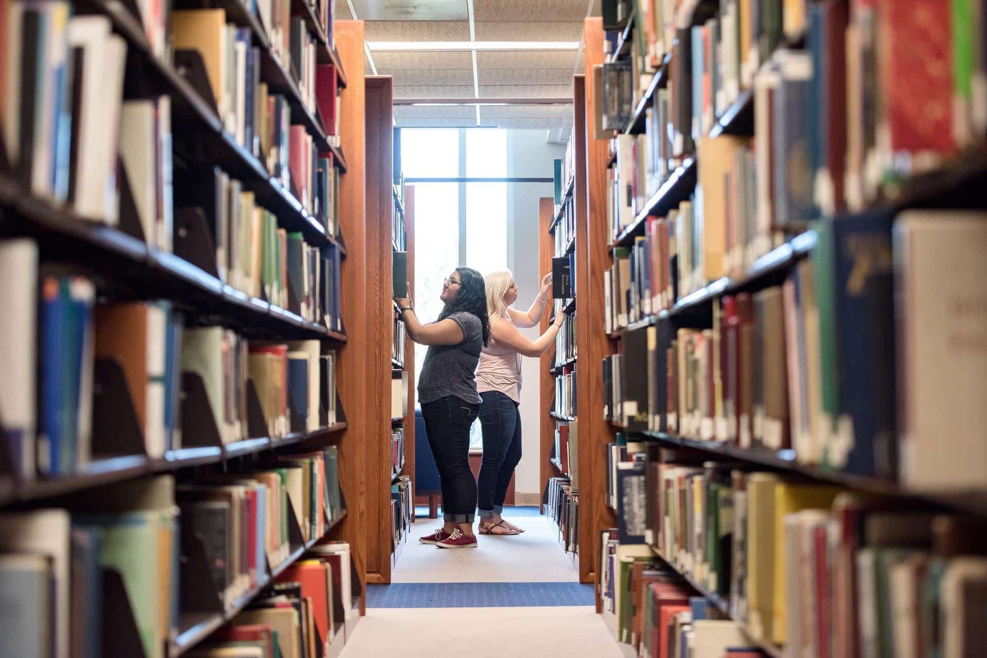 Two young women browsing for books in the library.
