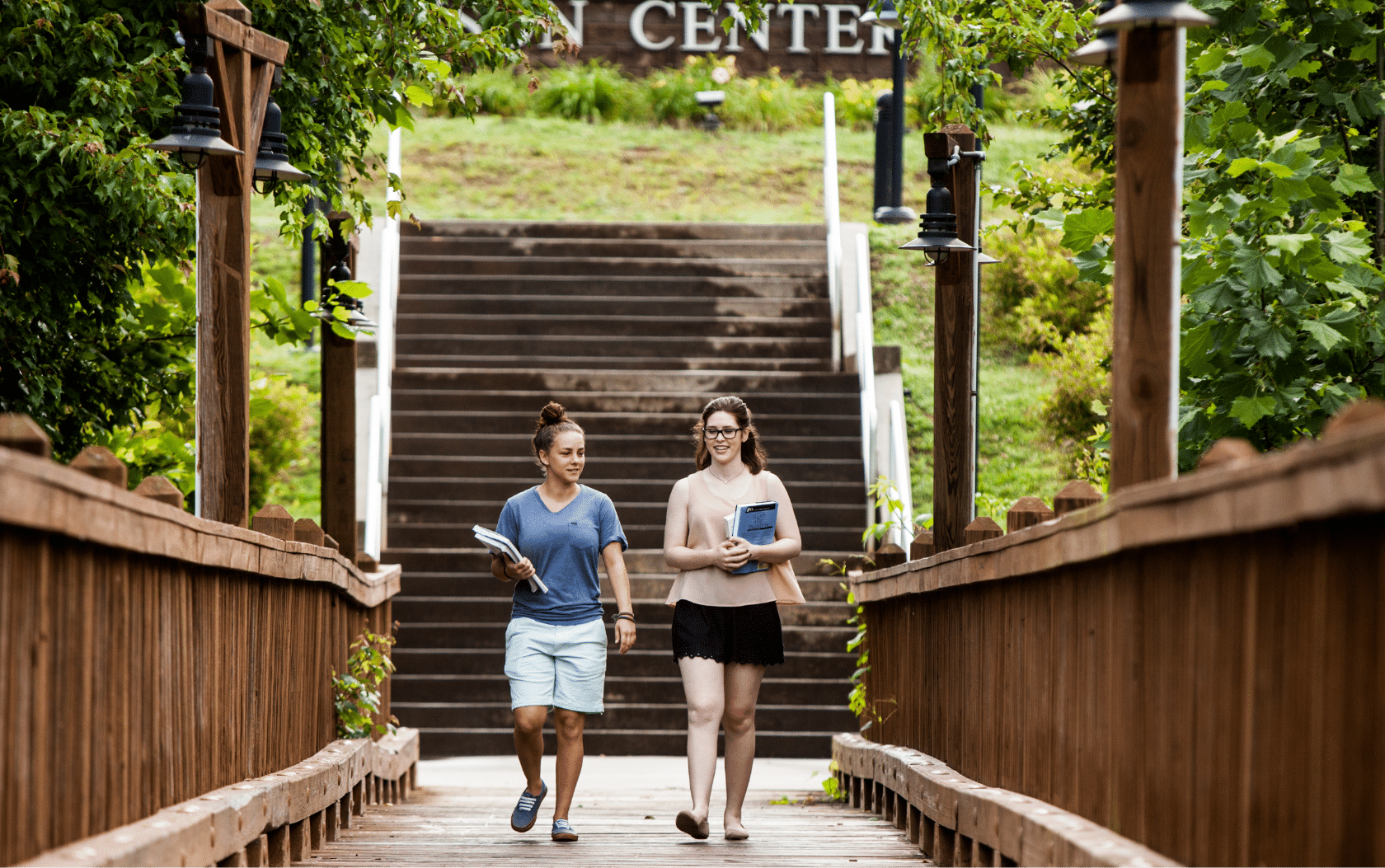 Two young women walking across a wooden bridge