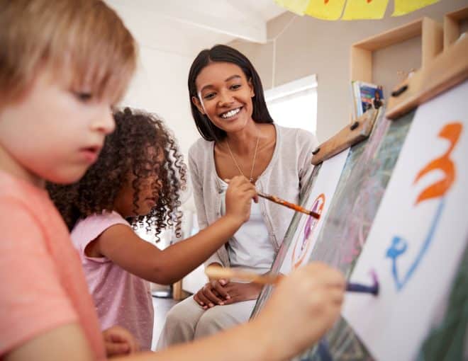 art teacher watching elementary school students paint on canvas