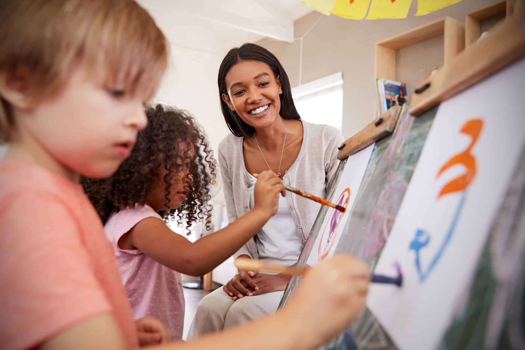 art teacher watching elementary school students paint on canvas