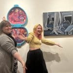 Two women posing in front of canvas art on the wall