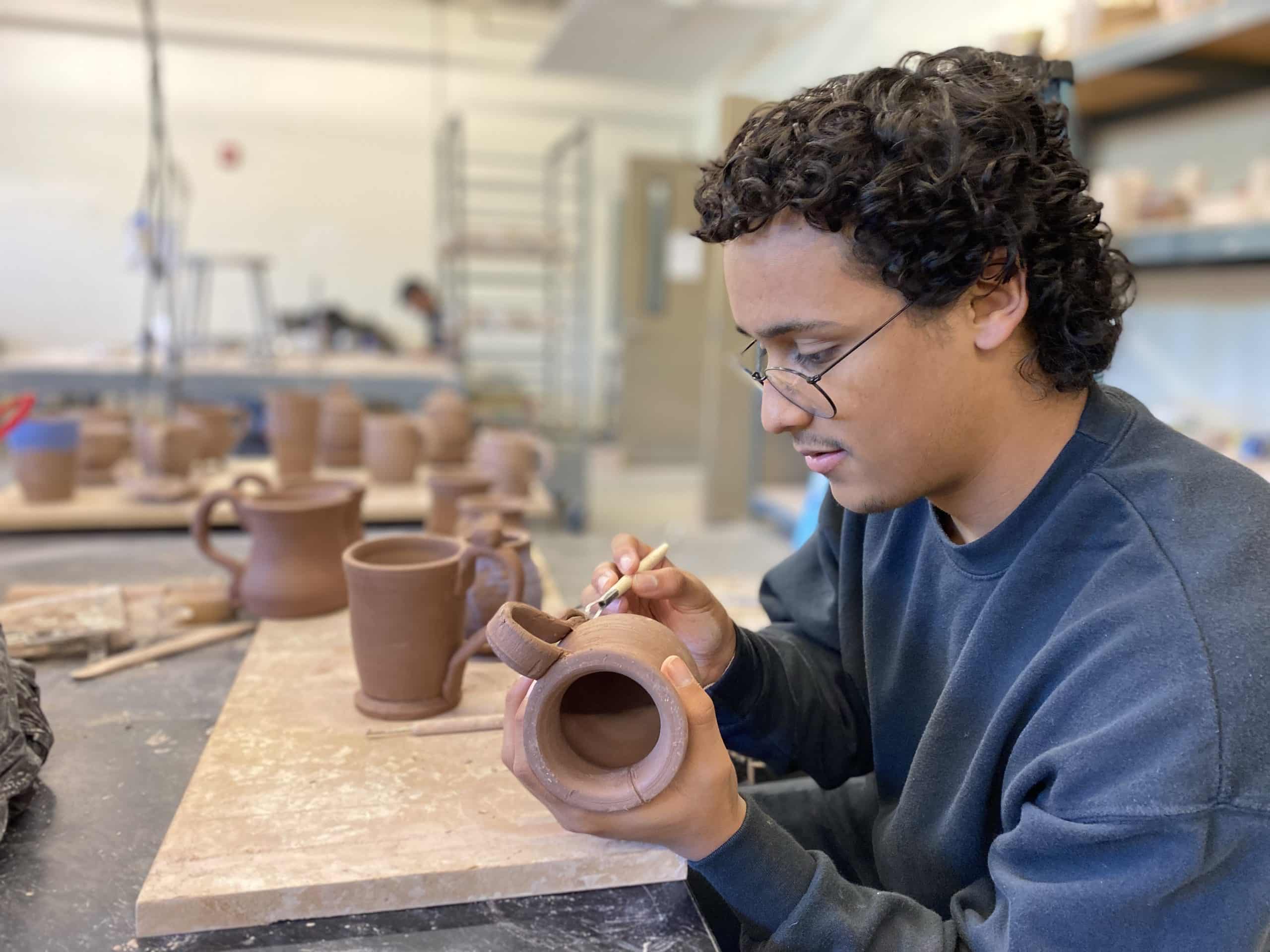 Young man adding details to an unfired ceramic mug