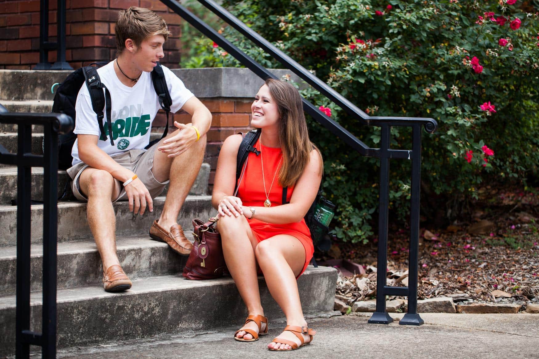 Young man and young woman sitting on stairs together, talking and laughing.