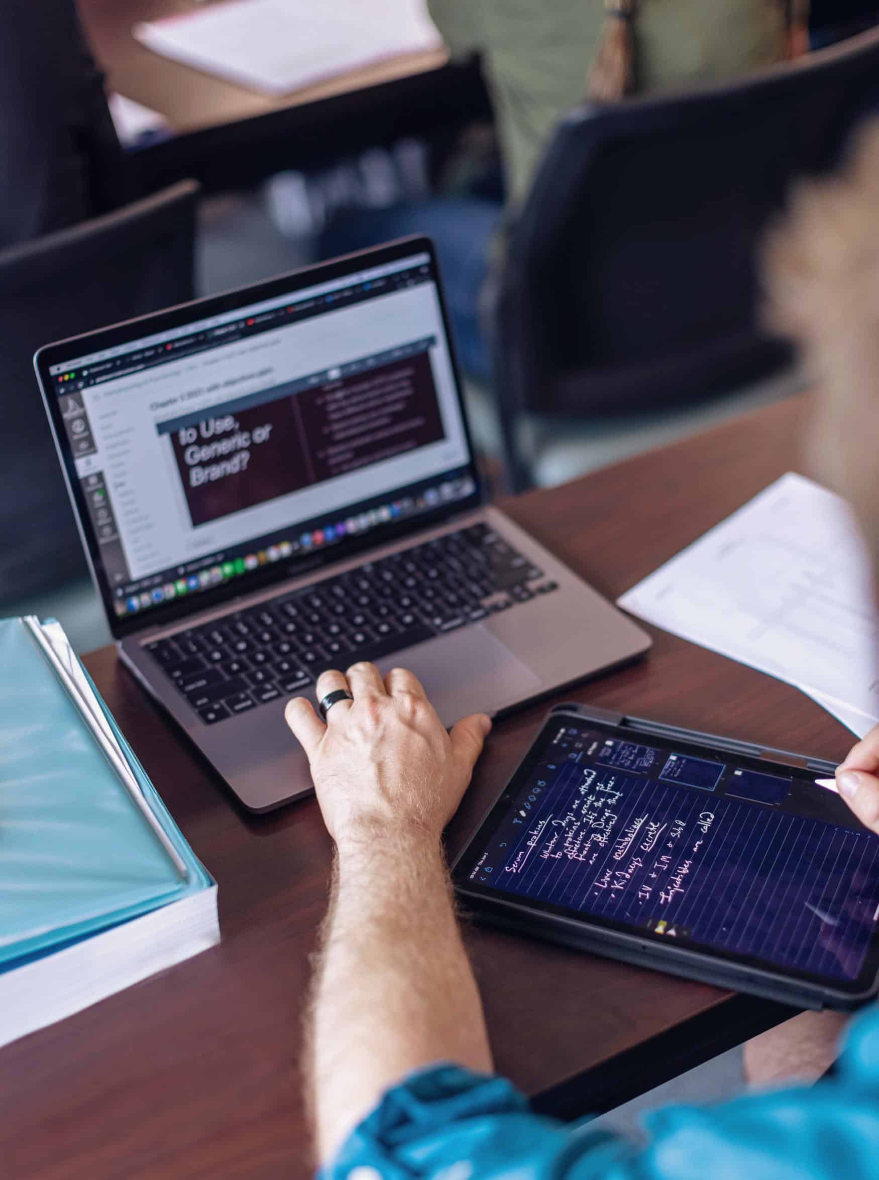 View of a person working on a laptop and a tablet with a writing tool