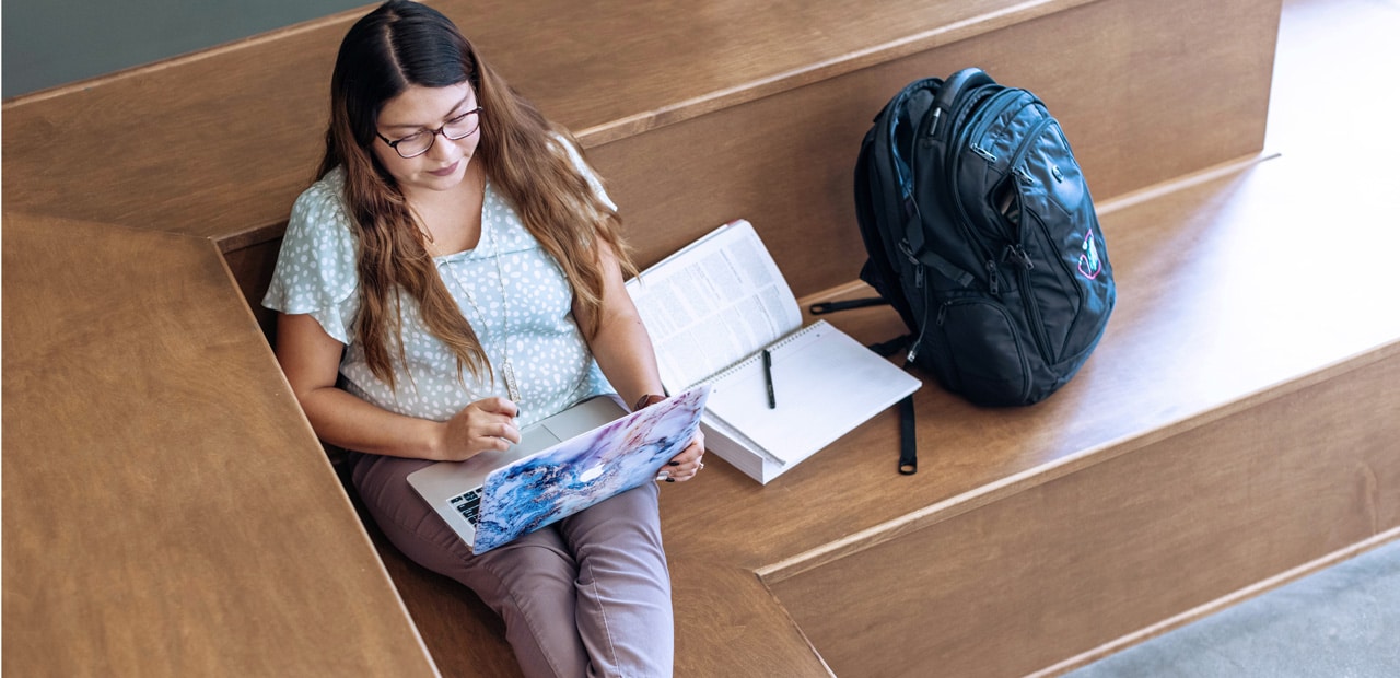 Young woman sitting on a wooden bench with a laptop and bookbag