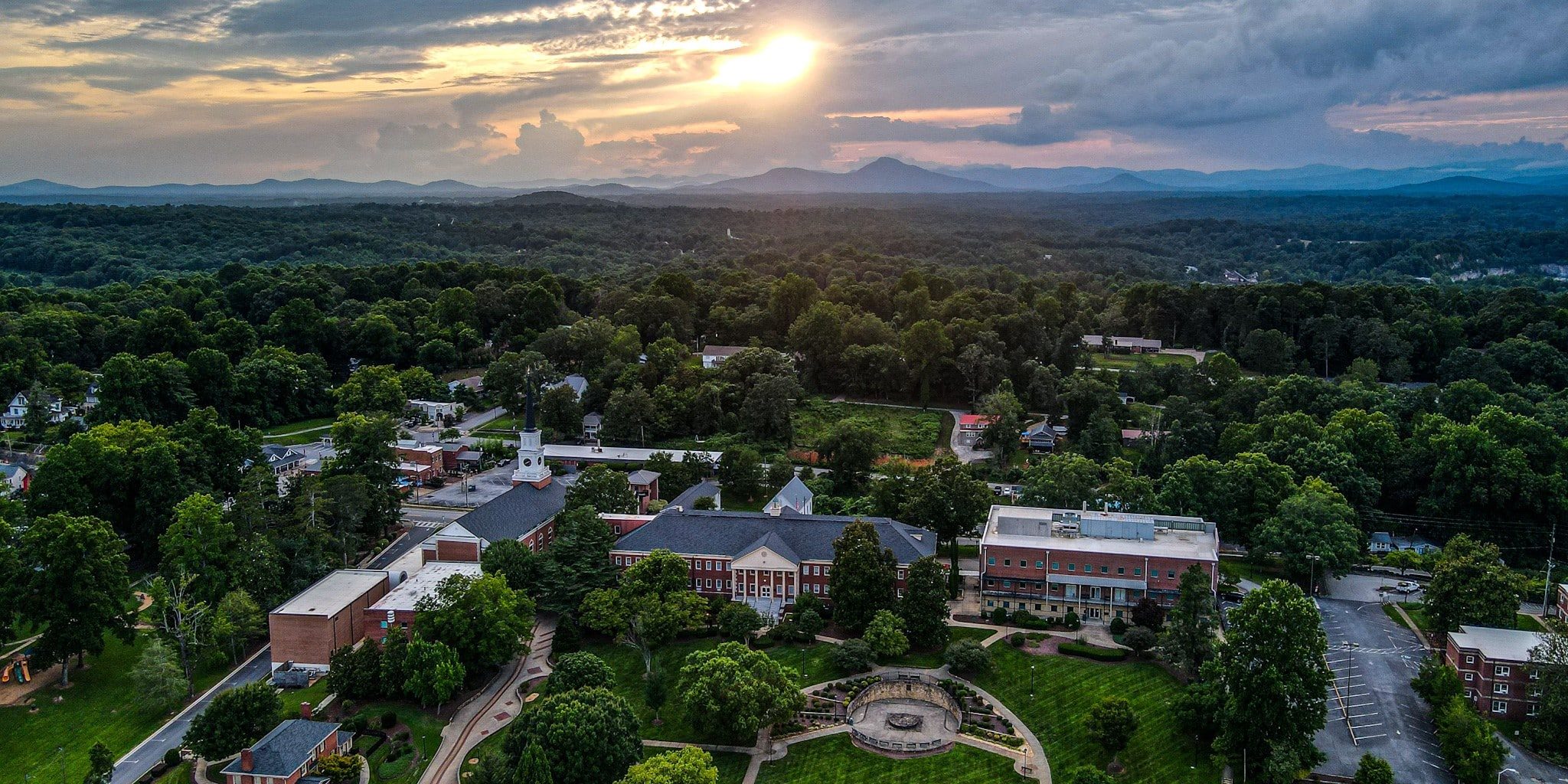 Aerial view of the Piedmont Demorest campus. Sun breaks through the clouds and mountains can be seen in the background.